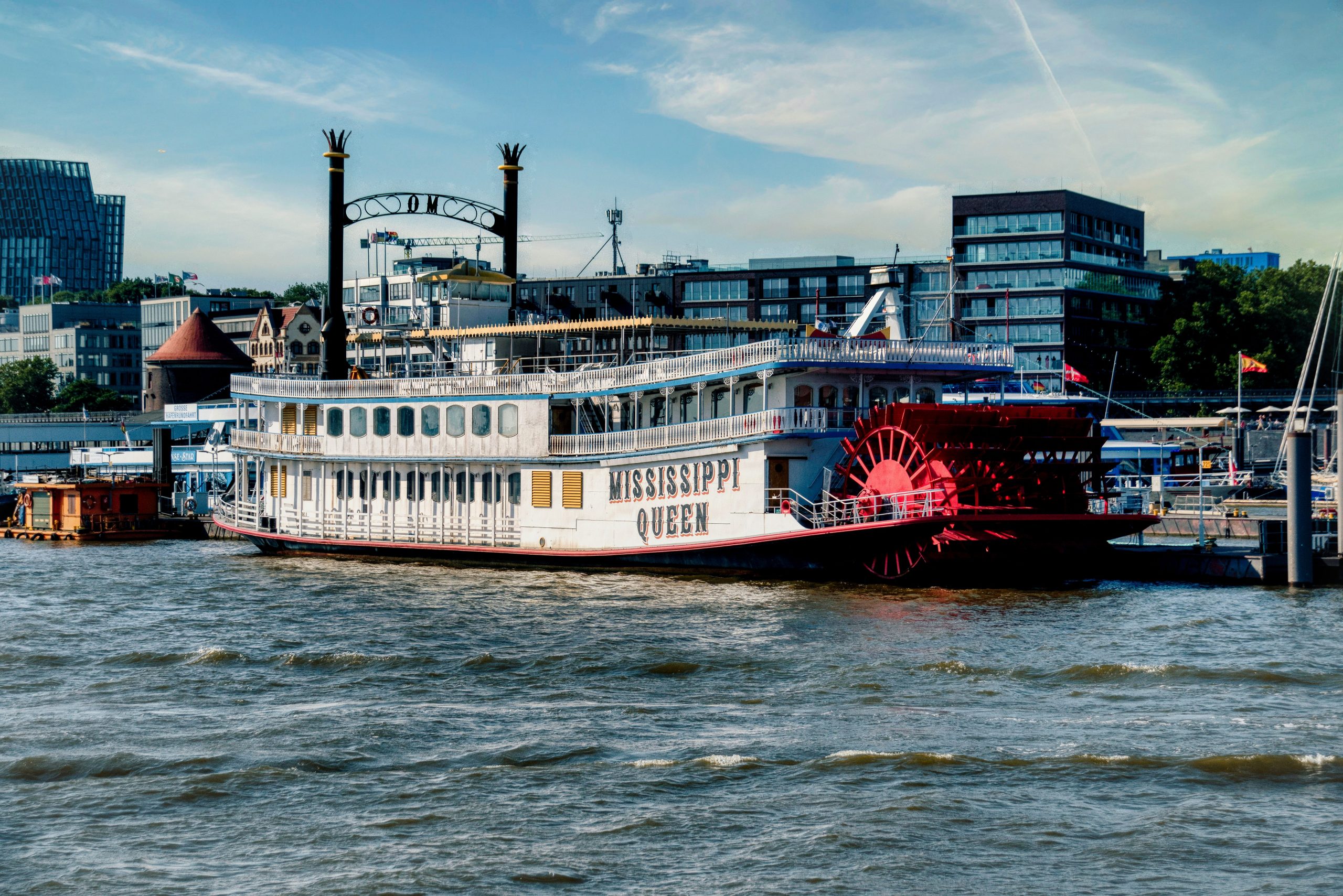 Elegant paddle steamer Mississippi Queen docked at urban waterfront under clear skies.